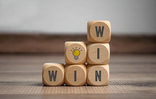 wooden blocked with the words "win win" on them stacked on top of each other with another wooden block that has a yellow light blub on it